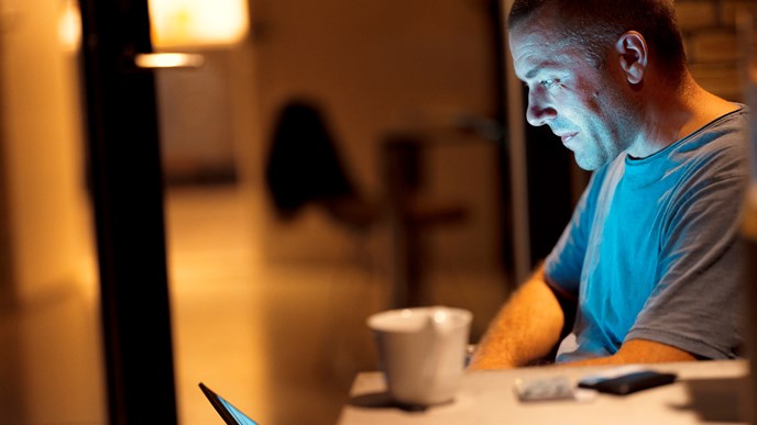 En mand kigger på sin computer og pensionsopsparing i aftenlysets skær