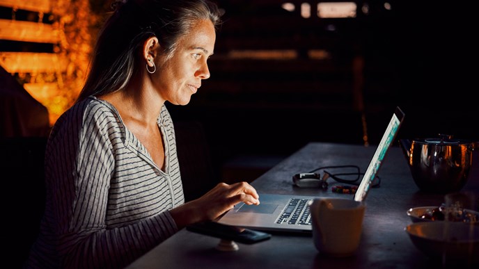 En kvinde tjekker sin pensionsopsparing på sin computer om aftenen på sin terrasse