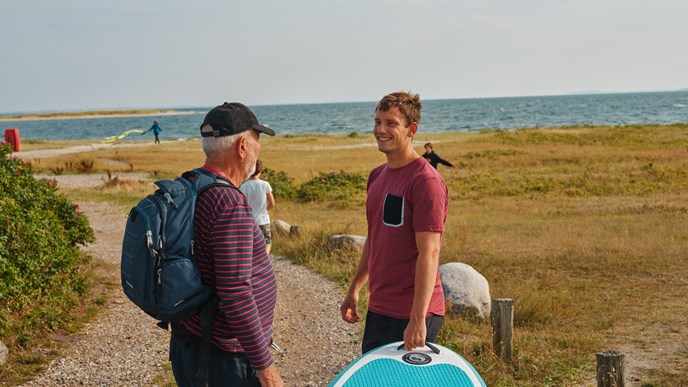 Pensioneret bedstefar og barnebarn med surfbræt og rygsæk ved strand