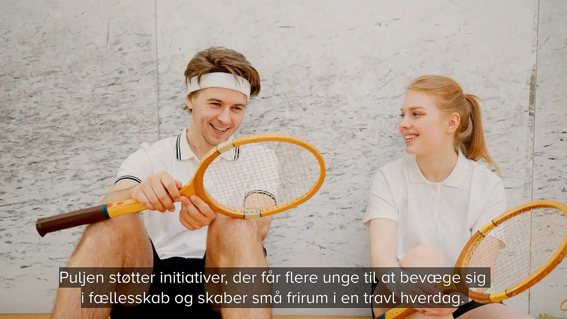 To unge tennisspillere ler sammen i pausen