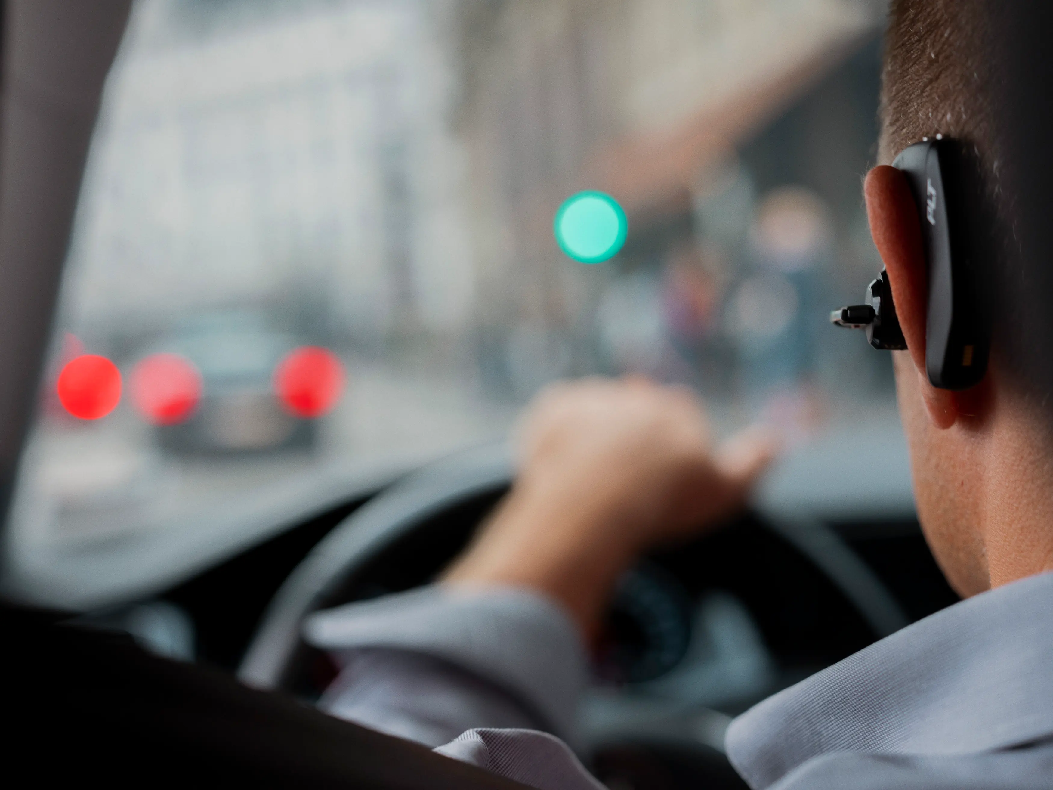Mand kører bil og snakker med bluetooth-enhed i øret
